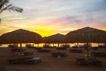 Tops of beach umbrellas made of natural materials isolated over blue and orange sky background. Photo shot at sunrise time. Horizontal color image.