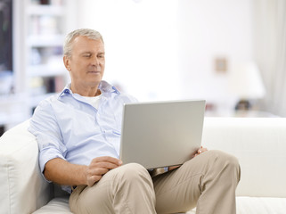 Browsing on the internet. Shot of a senior man using his laptop while relaxing at home. 