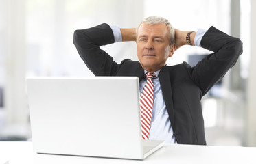 Professional financial man. Shot of a senior businessman working on laptop while sitting at office desk. His hands behind head.