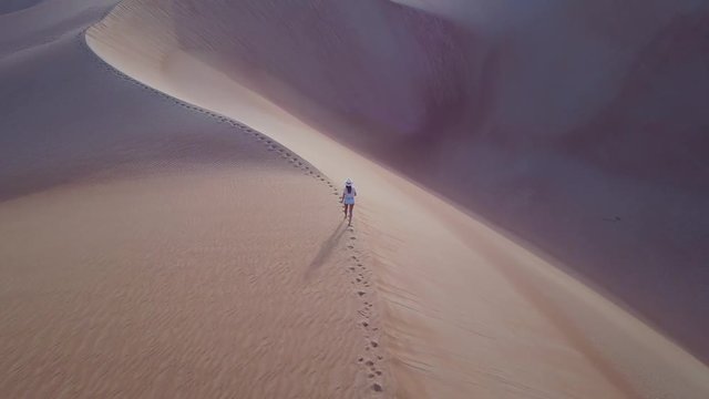 A woman walking on a sand dune during sunrise as viewed from a drone. Liwa desert, United Arab Emirates.