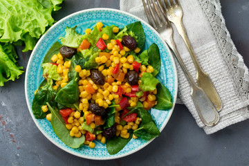  Warm salad with corn, pepper, olives and lettuce on a blue ceramic plate on a dark background. Selective focus.Top view.