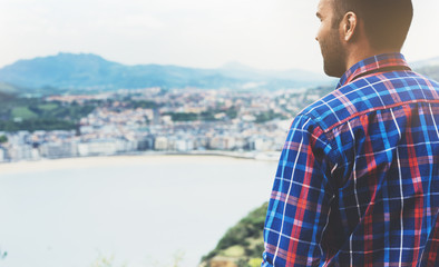 Hipster young man looking on observation deck in trip holiday in Bilbao, enjoying view on seascape on mountain and ocean, tourist traveler on background panoramic view of the city. Mock up for text