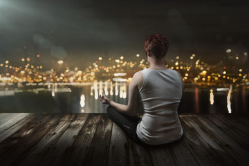 Frau meditiert am nächtlichen Stadtsee