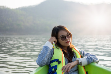 young woman equip life jacket sitting relaxing on prow. she looking side around herself have sea and sunset background. this image for travel,nature and portrait