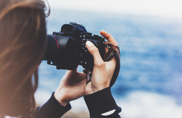 Tourist traveler photographer girl taking pictures of seascape on modern photo camera on background blue ocean view mockup sun flare, hipster female hands shoots video, nature holiday concept