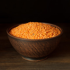 Raw red lentils in clay bowl on vintage wooden background.
