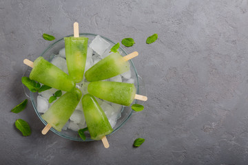 Homemade lime and mint leaves popsicles piled up on a plate of ice on grey concrete background. Top view, copy space
