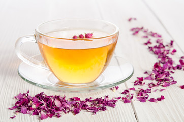 Glass cup of tea with rose petals on the white wooden background
