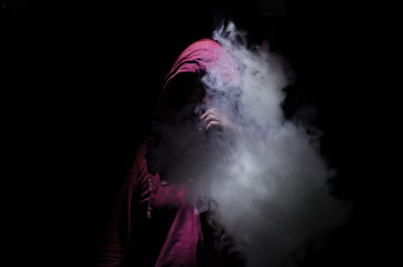 Vaping man holding a mod. A cloud of vapor. Black background. Vaping an electronic cigarette with a...