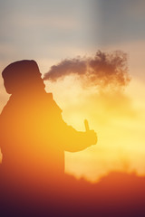 Close-up A man vape smokes an electronic cigarette against the sunset. The steam is falling....