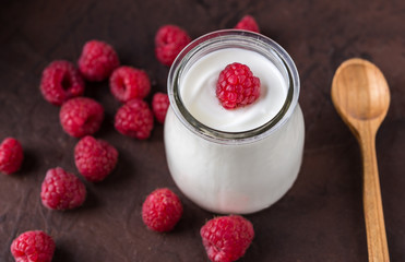 White yogurt with raspberries in glass bowl on rustic table.