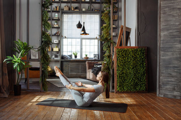 Young woman in homeware practicing balance yoga pose on carpet in her comfy bedroom.