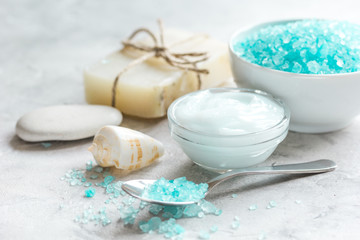 Fototapeta na wymiar blue bath salt, body cream and shells for spa on gray table background