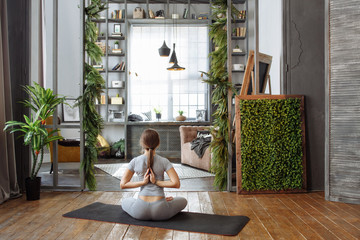Young woman in homeware practicing balance yoga pose on carpet in her comfy bedroom.