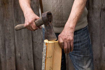 Worker, an elderly man with an old axe chops firewood. Forced to work in retirement . Employee .