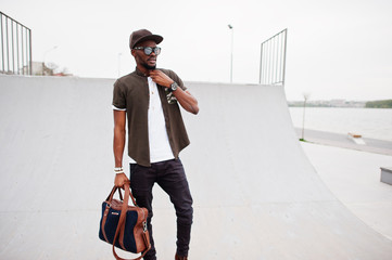 Portrait of sitting stylish african american man wear on sunglasses and cap with handbag outdoor...