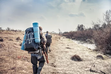 Fotobehang Jachtscène met jagers met rugzak en jachtuitrusting die tijdens het jachtseizoen door het landelijke gebied gaan © splendens