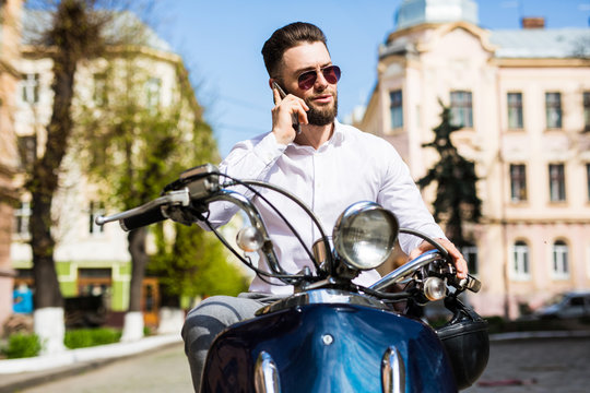 Cheerful young man sitting on scooter and talking on the mobile phone