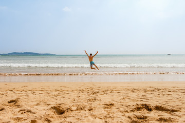 Man jumps on ocean sand beach. Happiness, holiday, travel concept.