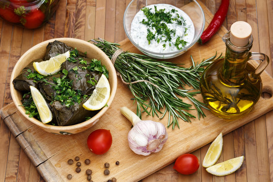 Dolma served with slices of lemon, cilantro, sour cream sauce with garlic on a wooden board. Olive oil with rosemary.
