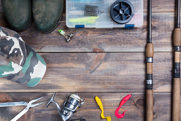 Fishing rods and reel with boots, cap and fishing tackles in a box on wooden background with free...