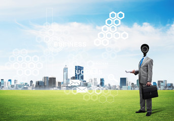 Camera headed man standing on green grass against modern cityscape