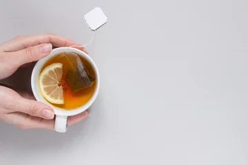 Foto auf Acrylglas Teezeit. Hände, die eine Tasse heißen schwarzen Tee auf blauem Hintergrund halten, Ansicht von oben © fedorovacz