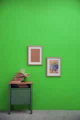 Bedside table with books and paintings on greenery wall background