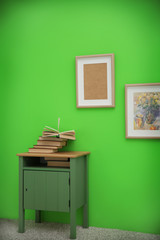 Bedside table with books and paintings on greenery wall background