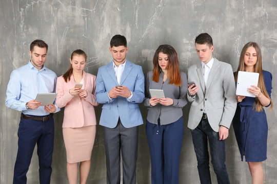 Young people in business clothes using digital devices on gray textured background - Powered by Adobe