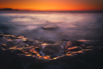Dark seascape with sunset reflections on rocks