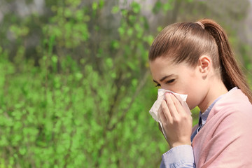 Sneezing young girl with nose wiper among blooming trees in park