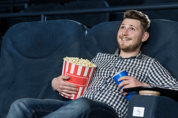 Young cheerful handsome guy enjoying a movie at the cinema