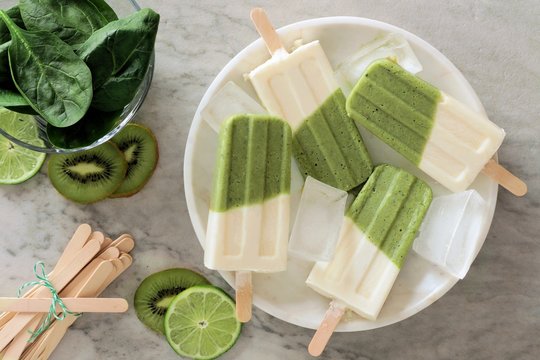 Green smoothie popsicles with kiwi, lime and spinach on a white marble plate, above view