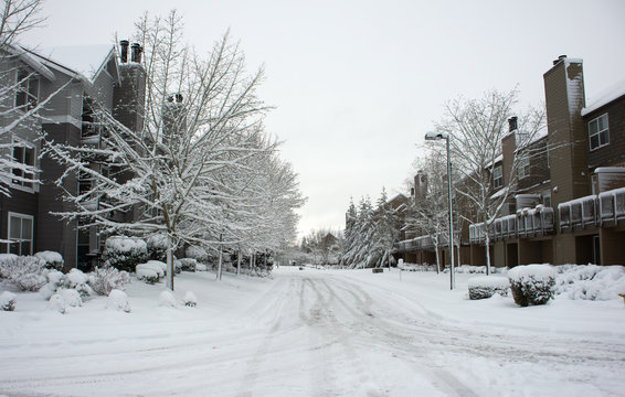 A snow covered residential roadway between two residential apartment buildings