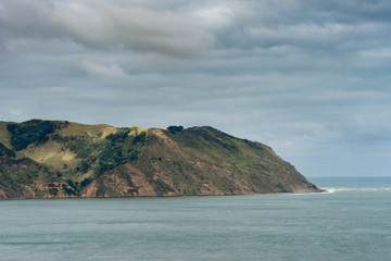 Auckland, New Zealand - March 2, 2017: Manukau Heads at entrance from Tasman Sea into Huia Bay. under heavy cloudscape. Blue-green water.