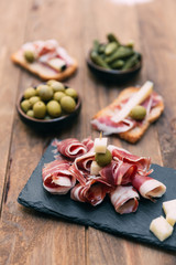 Spanish tapas with slices jamon serrano, salami, olives and cheese cubes on a wooden table. Spanish cuisine.