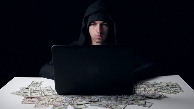 A hacker in a hood earns money. Cyber crime.