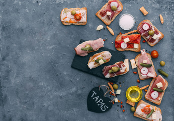 Still life, food and drink, holidays concept. Assortment of spanish tapas or italian antipasti, jamon, prosciutto, chorizo, salami on a grunge black board, rustic style.