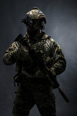 Bearded soldier in Combat Uniforms with weapon, plate carrier and combat helmet are on. Studio shot, dark background