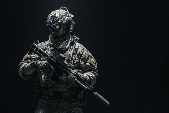 Army soldier in Combat Uniforms with assault rifle, plate carrier and combat helmet are on, Shemagh Kufiya scarf on his neck. Studio shot, dark background