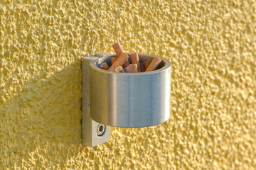 Wall-mounted stainless steel cigarette bin on an exterior wall outside a place of work where...