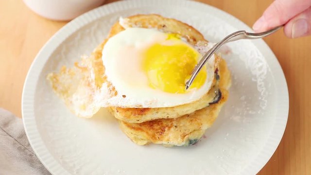 An older man prepares to eat a fried egg atop blueberry pancakes