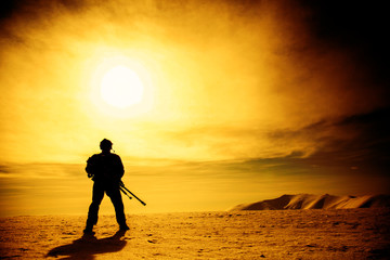Silhouette of soldier with sniper rifle standing under scorching sun in the mountains