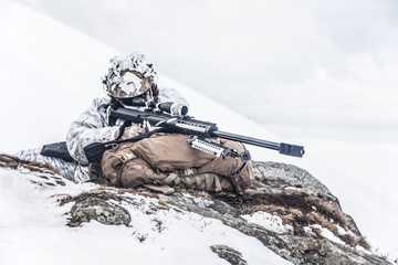 Army soldier with Sniper rifle in action in the Arctic. He lies among the cold rocks and stones,...