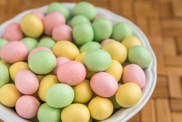 Bowl of pastel Easter candy eggs in a white bowl on a wood background
