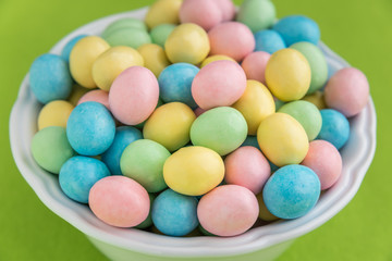 Bowl of pastel Easter candy eggs in a white bowl on a green background
