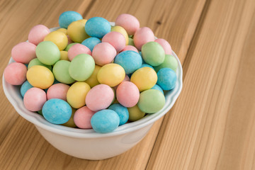 Fototapeta na wymiar Bowl of pastel Easter candy eggs in a white bowl on a wood background 