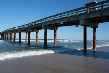 Obraz premium St Augustine, Florida, USA - 20 March 2017: St Augustine Beach Florida on a sunny day with no clouds. Water laps around wood pier. People enjoying St Johns County Ocean Pier.