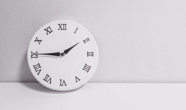 Closeup white clock for decorate show a quarter to two o'clock or 1:45 p.m. on white wood desk and wallpaper textured background in black and white tone with copy space
